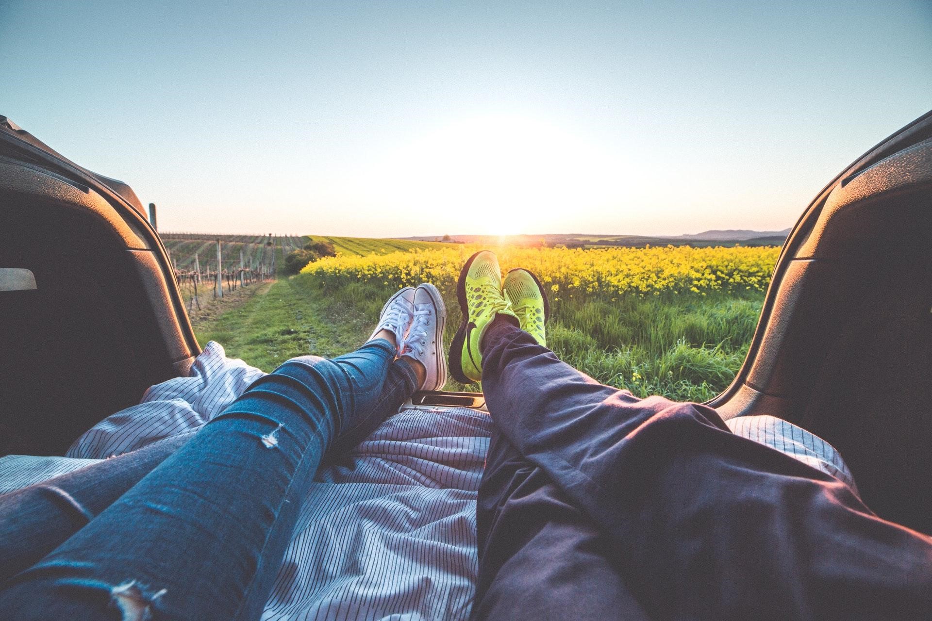 A couple sitting in the back of their truck watching the sunset over a meadow
