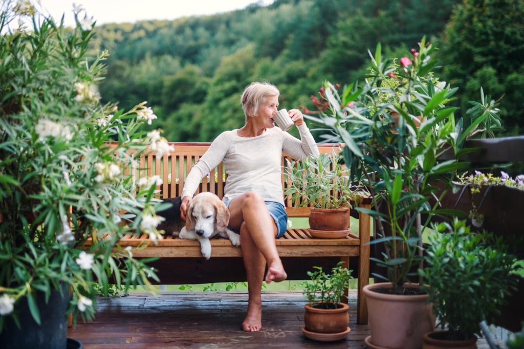 Older woman sitting on a bench with her dog on the deck sipping coffee
