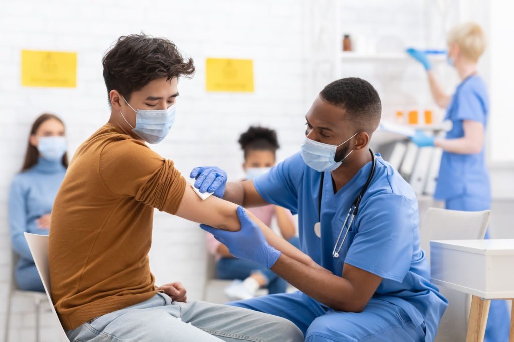 African American nurse administering a shot to a young male
