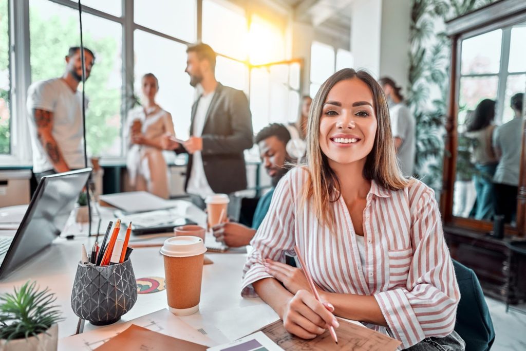 Smiling young adult business woman in the workspace with coworkers