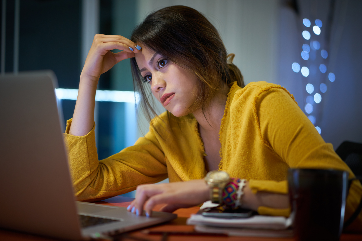 Young woman with laptop computer for homework. Tired hispanic girl and college education. Female student studying and using pc at home getting headache