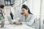 asian-woman-working-on-laptop-businesswoman-busy-working-on-laptop-computer-at-office-with-colleagues-in-the-background-stockpack-gettyimages
