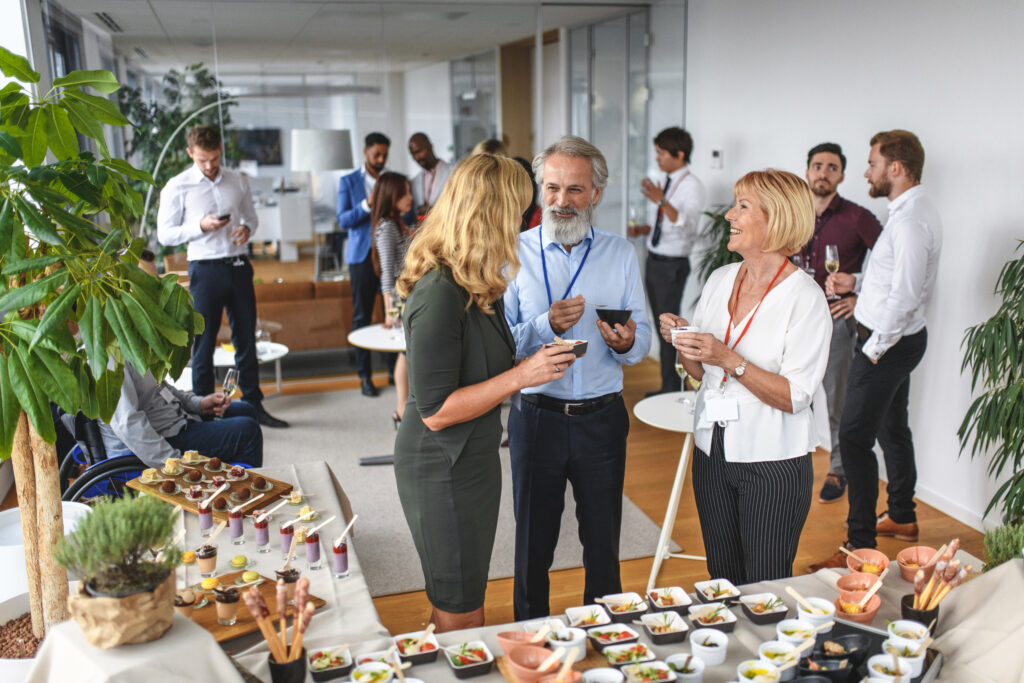 Elevated viewpoint of relaxed corporate colleagues enjoying savory dishes from buffet table at party to celebrate launch of new business.