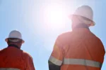 Two unrecognizable blue collar workers isolated against clear blue sky with sun flare.Real people. Copy space